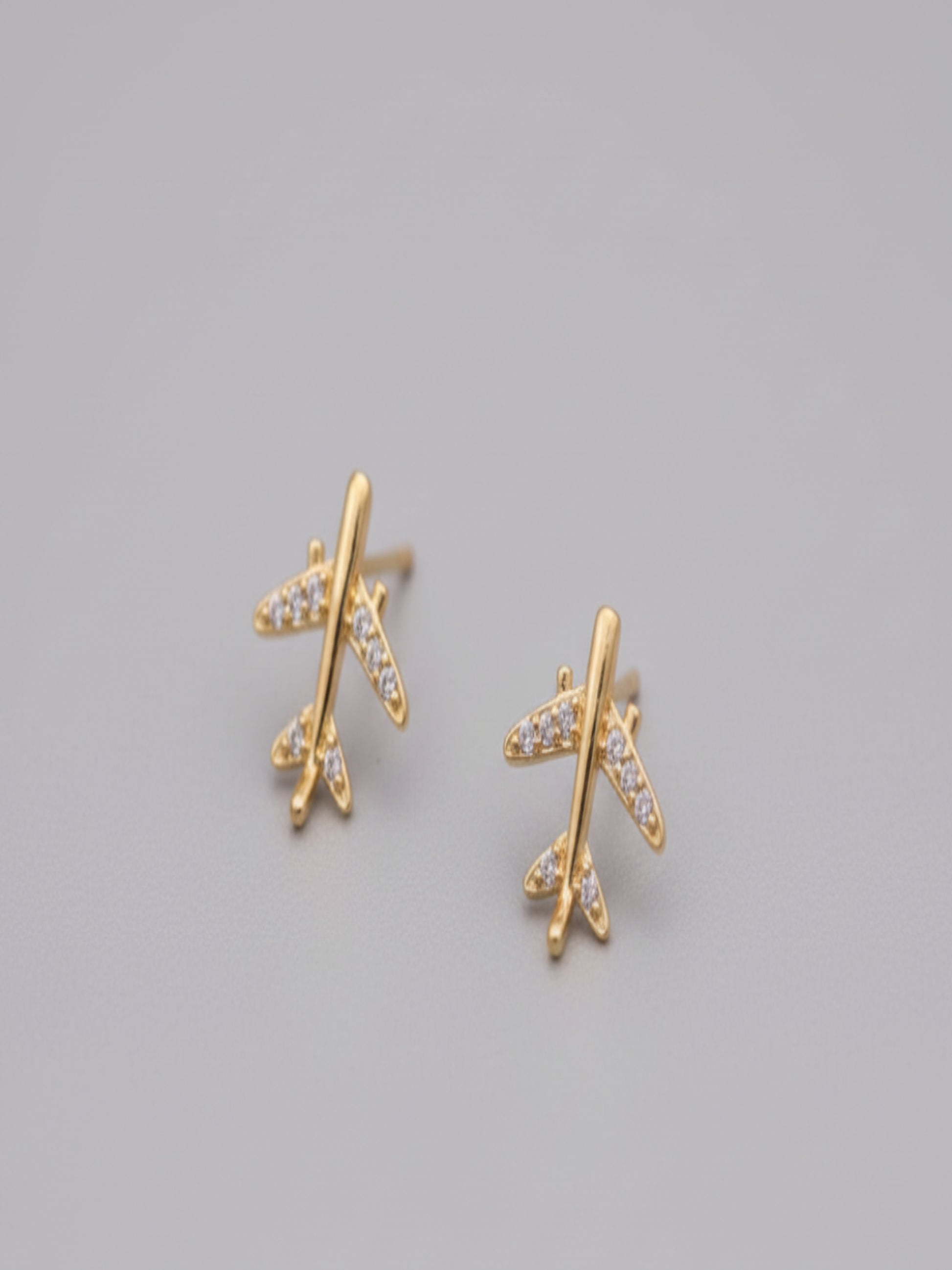 Gold airplane-shaped earrings on a brown surface